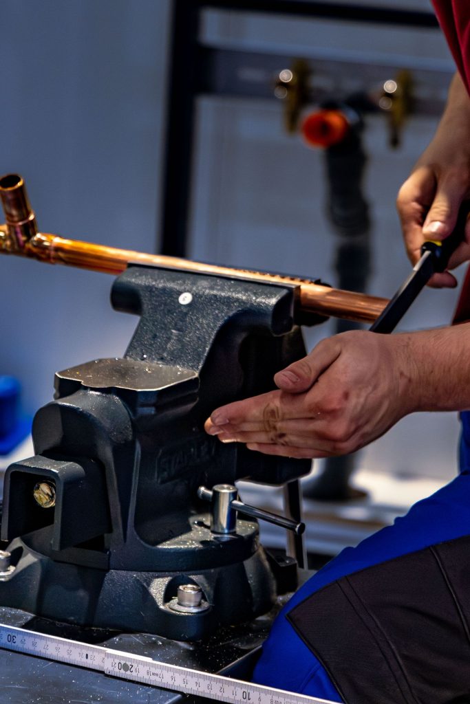 Plumber bending a copper pipe with a pipe bender in a workshop