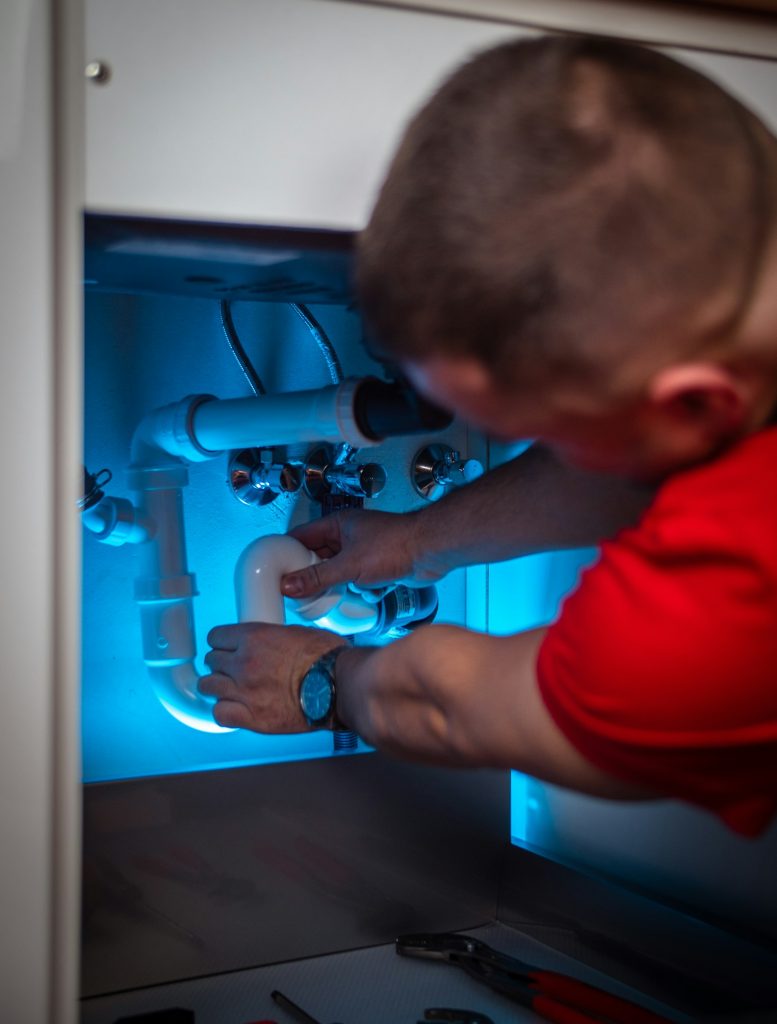Technician repairing a pipe connection inside a sink cabinet