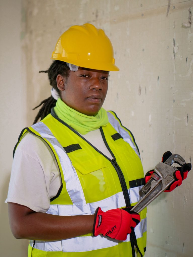 Plumbing technician in safety vest and helmet holding a pipe wrench
